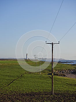 A row of wooden Telegraph poles crossing a field at Usan towards the Scurdie Ness lighthouse in the distance.