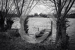 a rowboat lies on the shore of a lake in black and white