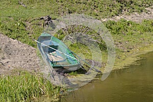 A rowing fishing boat lying on the shore of a reservoir, pulled ashore.