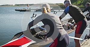 Rowing team of four senior caucasian men and women lowering boat into river