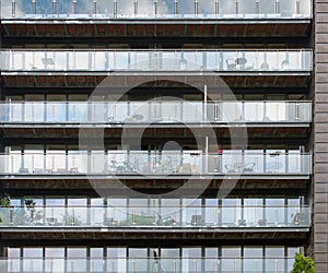 Rows of apartments in a large modern building with glass balconies and outdoor furniture and sky reflected in the windows