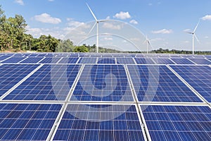 Rows array of polycrystalline silicon solar panels and wind turbines generating electricity in hybrid power plant systems station