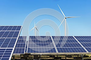 Rows array of polycrystalline silicon solar panels and wind turbines generating electricity in hybrid power plant systems station