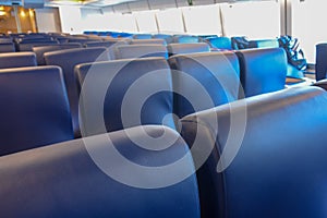 Rows of blue seats, elegant lounge inside a ferry. Comfortable chairs, windows in background