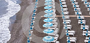 Rows of blue and white parasols and sunbeds on the beach at Atrani on the Amalfi Coast, Italy.