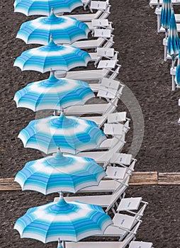 Rows of blue and white parasols and sunbeds on the beach at Atrani on the Amalfi Coast, Italy.