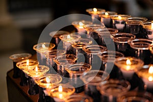 Rows of burning votive candles in a dark European Catholic church in Rome Italy seeking favor from the Lord or saint