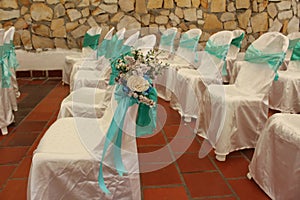Chairs arranged for a wedding ceremony on a brick red tile floor with turquoise sashes and flowers decorating them photo
