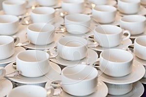 Rows of clean white coffee or tea cups, dish and spoon in a cafeteria or restaurant ready to serve a hot beverage