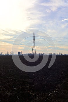 Rows of electricity pylons and power lines over cultivated fields on a winter day in the italian countryside