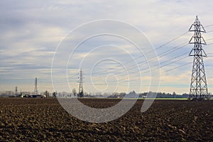 Rows of electricity pylons and power lines over cultivated fields on a winter day in the italian countryside