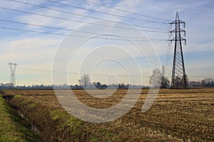 Rows of electricity pylons and power lines over cultivated fields on a winter day in the italian countryside