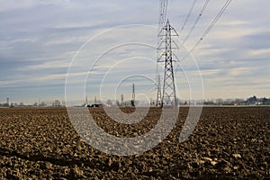 Rows of electricity pylons and power lines over cultivated fields on a winter day in the italian countryside