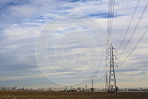 Rows of electricity pylons and power lines over cultivated fields on a winter day in the italian countryside