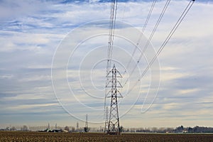 Rows of electricity pylons and power lines over cultivated fields on a winter day in the italian countryside