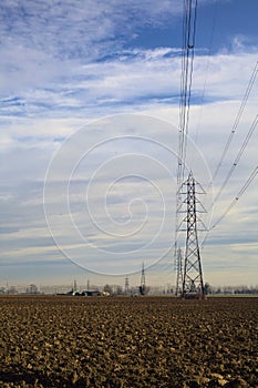 Rows of electricity pylons and power lines over cultivated fields on a winter day in the italian countryside