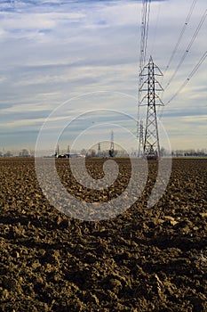 Rows of electricity pylons and power lines over cultivated fields on a winter day in the italian countryside