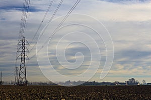 Rows of electricity pylons and power lines over cultivated fields on a winter day in the italian countryside