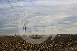 Rows of electricity pylons and power lines over cultivated fields on a winter day in the italian countryside