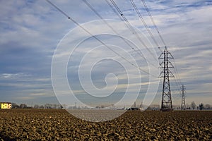 Rows of electricity pylons and power lines over cultivated fields on a winter day in the italian countryside