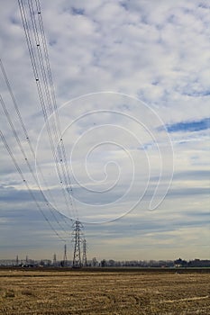 Rows of electricity pylons and power lines over cultivated fields on a winter day in the italian countryside