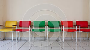 Rows of empty chairs in yellow, red and green. Plain wall background