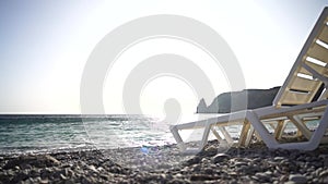 Rows of empty white plastic chair and sunbathing beds on beach near sea at sunset. Relaxation area for chilling out on