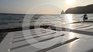 Rows of empty white plastic chair and sunbathing beds on beach near sea at sunset. Relaxation area for chilling out on