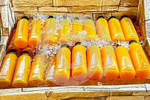 Rows of fresh orange juice in transparent bottles are chilled in water-filled, makeshift street cooler