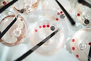 Rows of glasses with light pink beverage on buffet table top view. Close up of drink with fresh berries and straw