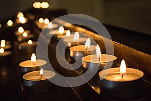 Rows of glowing candles in darkness. Candles with burning falme. Church decoration. Religion and faith background.