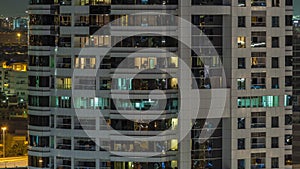 Rows of glowing windows with people in apartment building at night.