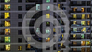 Rows of glowing windows with people in apartment building at night.