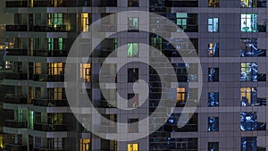 Rows of glowing windows with people in apartment building at night.