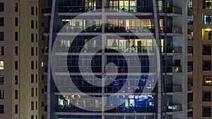 Rows of glowing windows with people in apartment building at night.