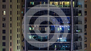 Rows of glowing windows with people in apartment building at night.