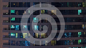 Rows of glowing windows with people in apartment building at night.