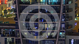 Rows of glowing windows with people in apartment building at night.