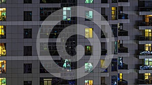 Rows of glowing windows with people in apartment building at night.