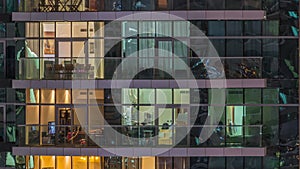 Rows of glowing windows with people in apartment building at night.