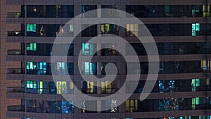 Rows of glowing windows with people in apartment building at night.