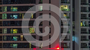 Rows of glowing windows with people in apartment building at night.