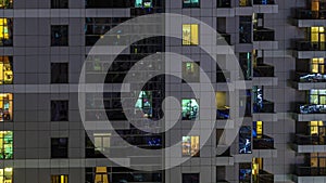 Rows of glowing windows with people in apartment building at night.