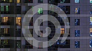 Rows of glowing windows with people in apartment building at night.