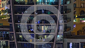 Rows of glowing windows with people in apartment building at night.