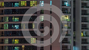 Rows of glowing windows with people in apartment building at night.