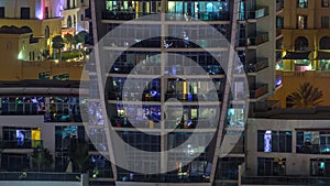 Rows of glowing windows with people in apartment building at night.