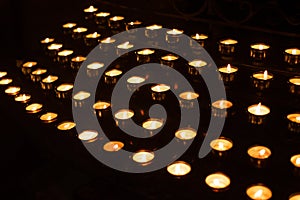 Rows of lighted prayer candles in the darkness in a church