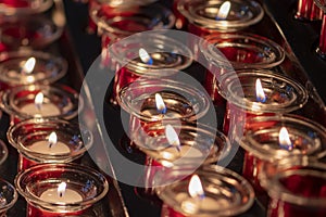 Rows of lit votive candles in a dimly lit room, the church\'s small round candles at Catholics. photo