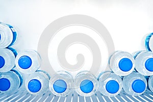 Rows of many transparent plastic bottles with drinking water supply in white refrigerator. Mineral water stack storage in fridge